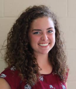 A smiling young woman with curly hair against a Howard Payne University background. | HPU