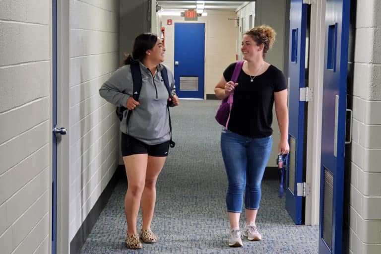 Two women engaged in conversation while walking in a hallway at Howard Payne University. | HPU