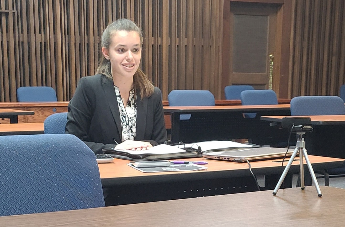 Woman sitting at a Howard Payne University conference table prepared to speak, with a microphone and a tripod-mounted device in front. | HPU