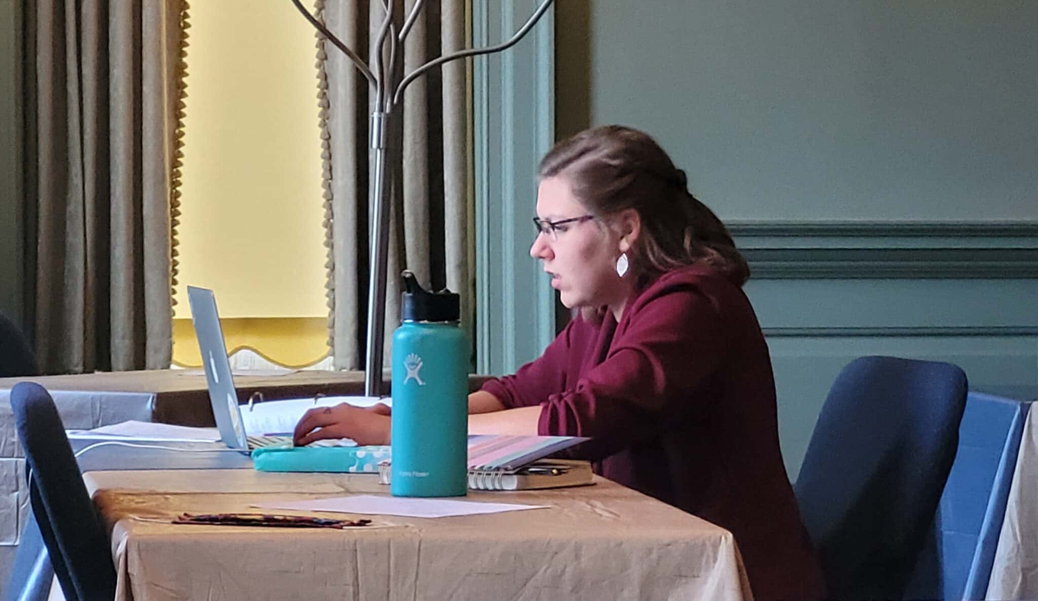 Woman concentrating on a Howard Payne University computer screen at a desk with a water bottle and notebooks beside her. | HPU
