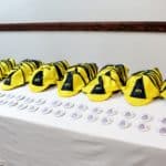 A row of Howard Payne University yellow and black striped graduation caps on a table with a set of diplomas placed in the foreground. | HPU