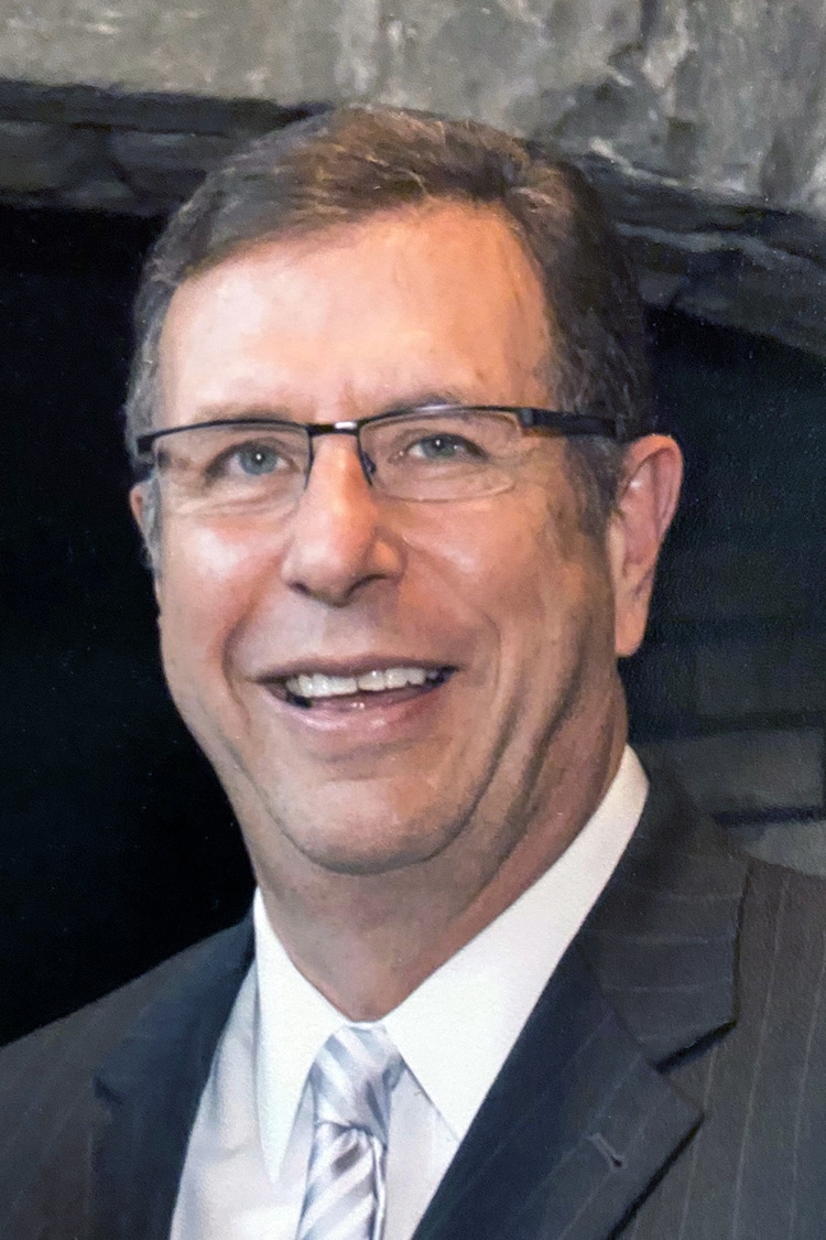 A smiling man wearing Howard Payne University glasses, a suit, and tie. | HPU