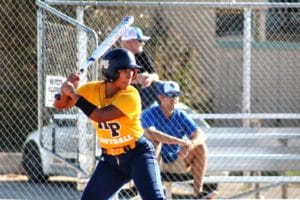 A Howard Payne University softball player in a yellow and blue uniform prepares to swing at an incoming pitch during a game. | HPU