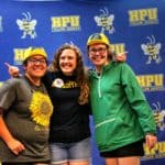 Three individuals smiling at a Howard Payne University event, wearing casual attire and novelty hats. | HPU