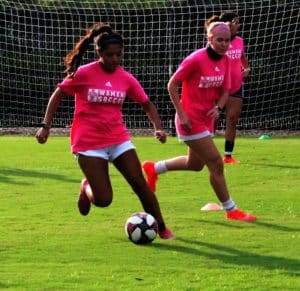 Two soccer players from Howard Payne University in pink jerseys practicing on the field. | HPU