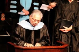 A man in graduation attire delivers a speech at a Howard Payne University podium. | HPU