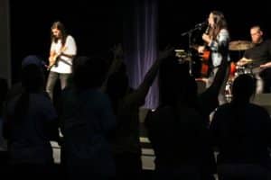 Musicians perform on stage at Howard Payne University as audience members raise their hands in a gesture of enjoyment or participation. | HPU