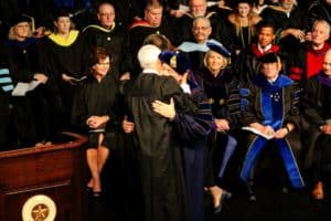 A Howard Payne University graduate being embraced at a commencement ceremony while others look on. | HPU