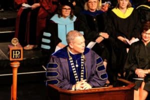A person in academic regalia speaking at a podium during a Howard Payne University graduation ceremony. | HPU