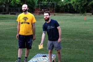 Two men standing on a grassy field at Howard Payne University with a game table between them, one holding a yellow flying disc. | HPU