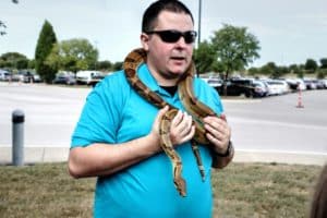 Man wearing sunglasses with a Howard Payne University shirt and a snake around his neck outdoors. | HPU