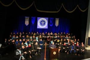 Graduation ceremony at Howard Payne University with students in cap and gown, and a speaker at the podium. | HPU