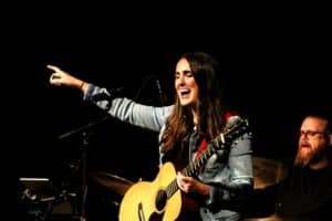 Female musician playing guitar and singing on stage at Howard Payne University while pointing into the audience. | HPU