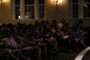 Howard Payne University audience members attentively watching a presentation in a dimly lit room. | HPU