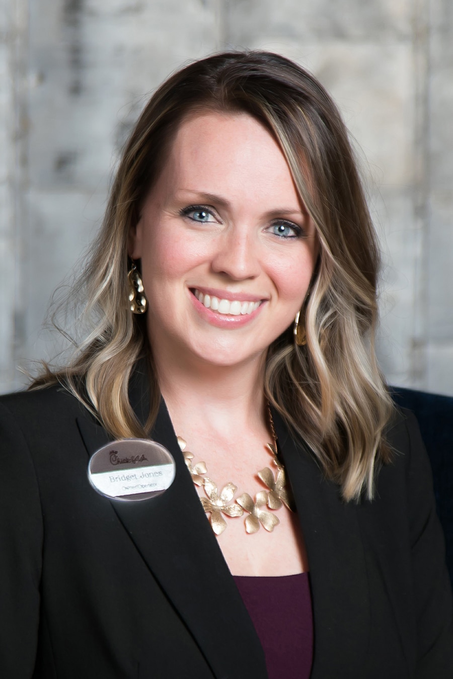 Professional portrait of a smiling woman with blond hair wearing a black blazer, a Howard Payne University name badge, and gold jewelry. | HPU