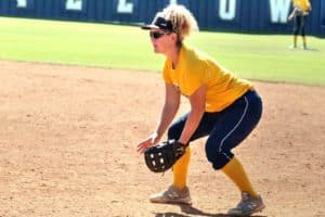 Softball player from Howard Payne University in yellow jersey crouched in readiness on the field. | HPU