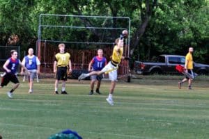 A person in yellow leaps to catch a football during an outdoor game at Howard Payne University while others run nearby. | HPU