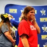 A person smiling with hand over mouth, wearing a red Howard Payne University shirt, being awarded a medal by another person in the background. | HPU