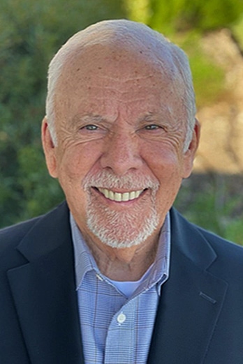 An elderly man with a smile, wearing a Howard Payne University suit jacket and a collared shirt, against a natural backdrop. | HPU