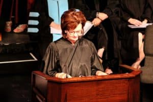 A person in judicial robes speaking at a lectern with others in similar attire from Howard Payne University in the background. | HPU