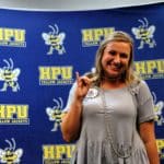 Woman posing with a 'number one' hand gesture in front of a Howard Payne University backdrop. | HPU