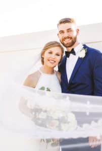 A smiling couple in Howard Payne University wedding attire; the bride holding a bouquet. | HPU