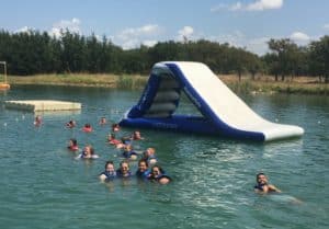 A group of Howard Payne University students in life jackets swimming near an inflatable water slide in a lake. | HPU