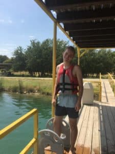 A young person wearing a Howard Payne University life jacket stands on a sunny dock by the water. | HPU