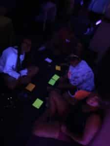 Friends socializing in a dark room with neon lighting and scattered glow sticks at Howard Payne University. | HPU