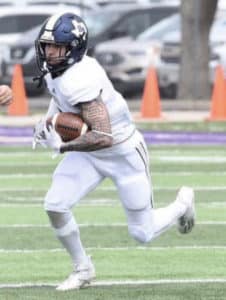 Football player from Howard Payne University in white uniform running with the ball during a game. | HPU
