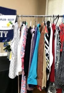 A variety of garments displayed on a clothing rack with a sign reading "plus-sizes" in Howard Payne University's background. | HPU