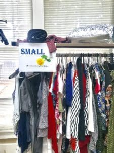 A cluttered clothes rack at Howard Payne University with a sign indicating "small" sizes, with various garments and a hat on the top shelf. | HPU