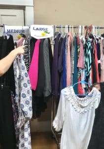 A person browsing through a rack of assorted clothes categorized by size at Howard Payne University. | HPU