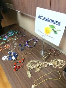 A variety of jewelry laid out on a surface with a sign labeled "Howard Payne University Accessories" featuring a rose image. | HPU