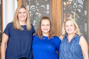 Three smiling women standing together in front of a door at Howard Payne University. | HPU