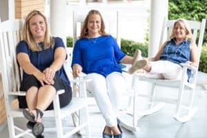 Three smiling women sitting in white rocking chairs on a Howard Payne University porch. | HPU
