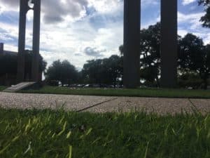 Low-angle view of Howard Payne University park with tall pillars and trees under a cloudy sky. | HPU