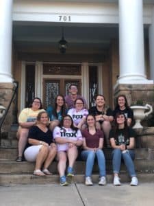 Group of people smiling on the front steps of a building at Howard Payne University with the address 701. | HPU