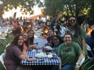 Outdoor community dining event hosted by Howard Payne University with people sitting at long tables and smiling at the camera. | HPU