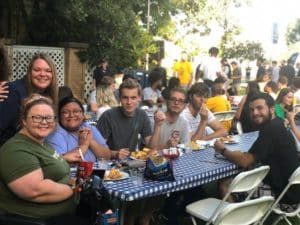 A group of Howard Payne University students enjoying a meal together outdoors at a table with a blue and white checkered tablecloth. | HPU
