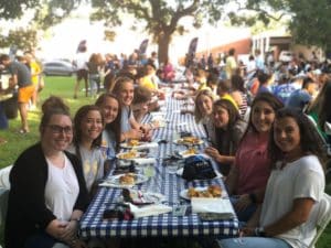 Group of Howard Payne University people enjoying an outdoor communal meal at a long table. | HPU