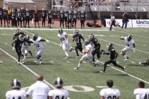 A Howard Payne University football game in action with players from two teams engaged on the field while others watch from the sidelines. | HPU