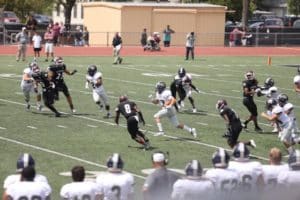 A football game in progress at Howard Payne University with a player carrying the ball while avoiding tackles. | HPU