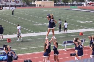 Cheerleaders from Howard Payne University performing a stunt with one cheerleader being lifted up by teammates on a football field. | HPU