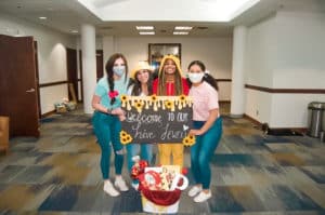 Four individuals wearing face masks posing with a Howard Payne University welcome sign and sunflower decorations. | HPU