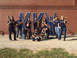 Group of people posing with baseball bats in front of a large "ky" sculpture at Howard Payne University. | HPU