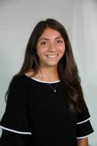 A smiling woman in a Howard Payne University black top with cut-out sleeve details against a light-gray background. | HPU
