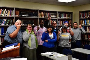 A group of people posing with various hand gestures in the Howard Payne University library setting. | HPU