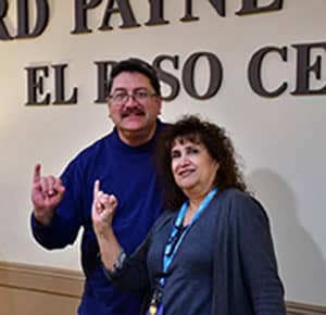 Two individuals smiling and gesturing with one hand each in front of a sign that reads "Howard Payne University el paso center. | HPU