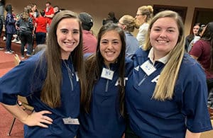 Three individuals in Howard Payne University blue uniforms with name tags, smiling for the photo. | HPU
